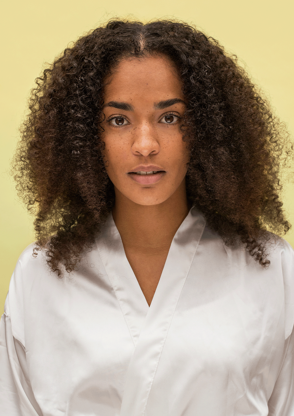 Woman with beautifully defined natural curls wearing a white robe, showcasing bouncy hair after using Curl Discovery Kit products.