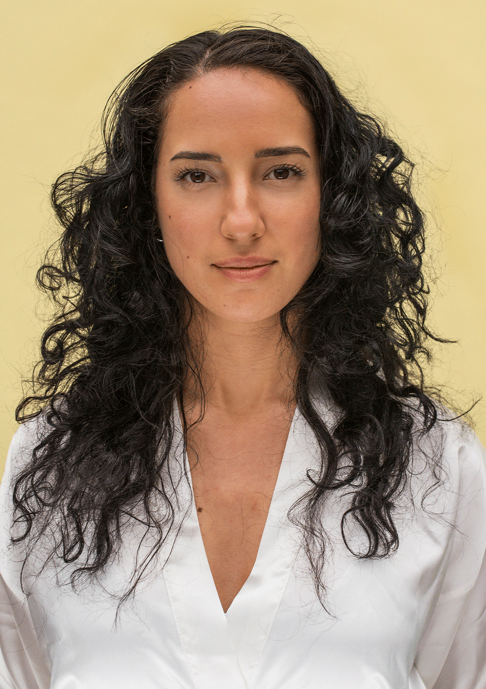 Woman with defined, bouncy curls using the Curl Discovery Kit, looking confident in a white shirt against a soft yellow background.