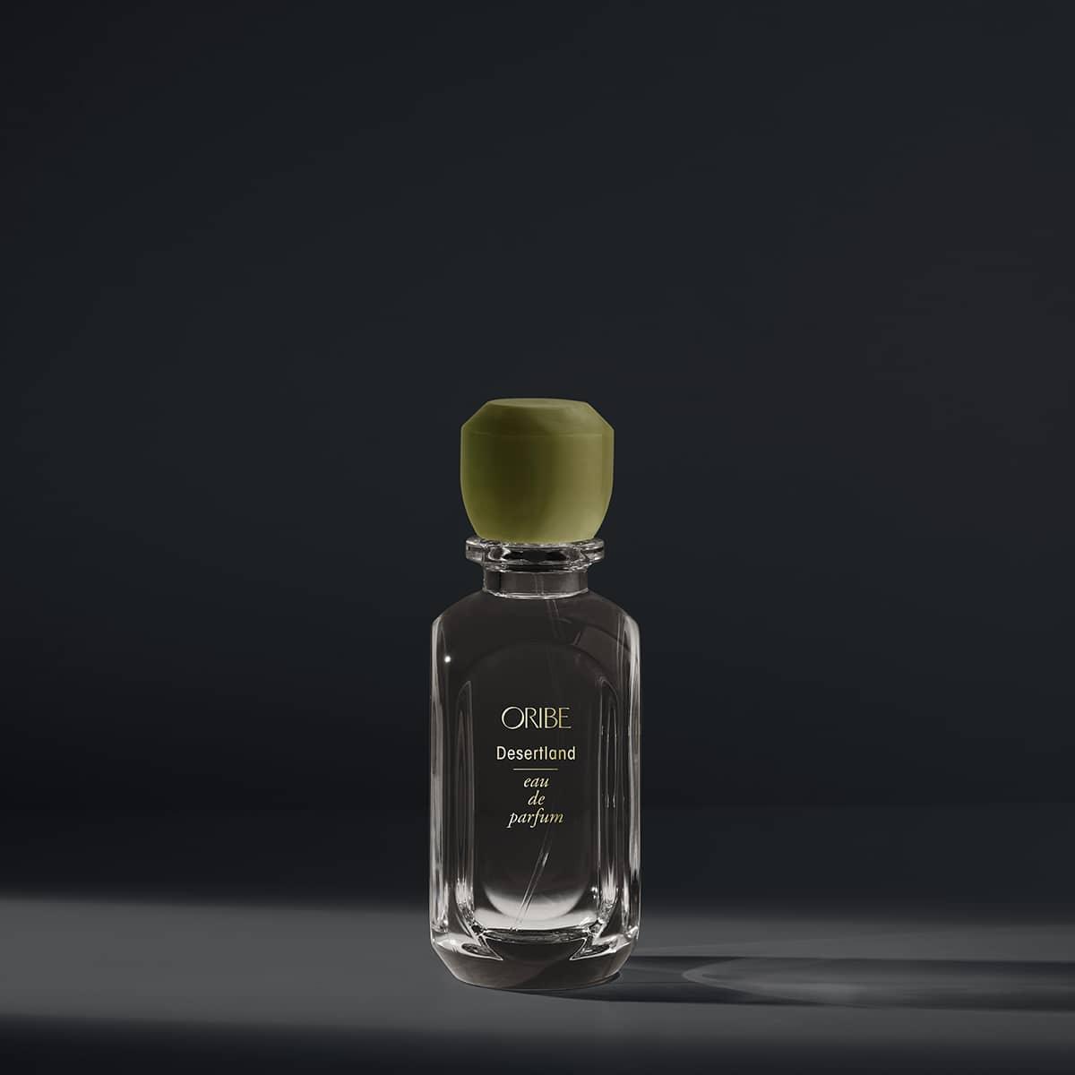 Desertland Eau De Parfum bottle with notes of juniper berry, lavender, pine, and cedarwood, set against a dark background.