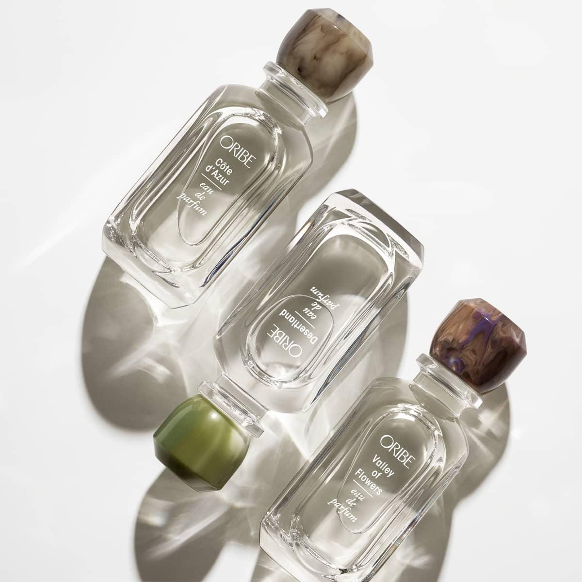 Elegant glass bottles of Desertland Eau De Parfum with colorful caps, casting soft shadows on a neutral background.