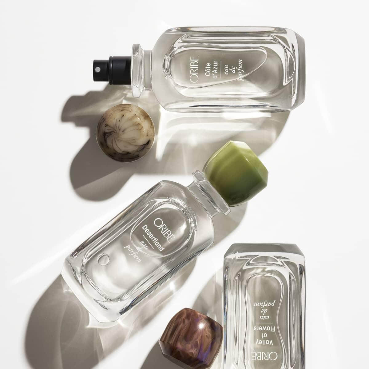 Three Desertland Eau De Parfum bottles on a reflective surface, highlighting the luxurious fragrance inspired by a vibrant desert essence.