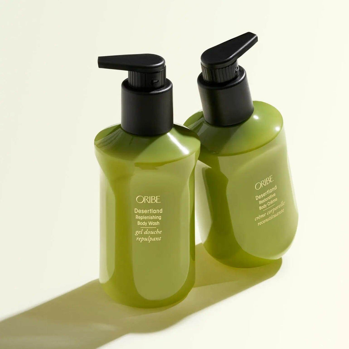 Two bottles of Oribe Desertland Replenishing Body Wash with pump dispensers on a light background.