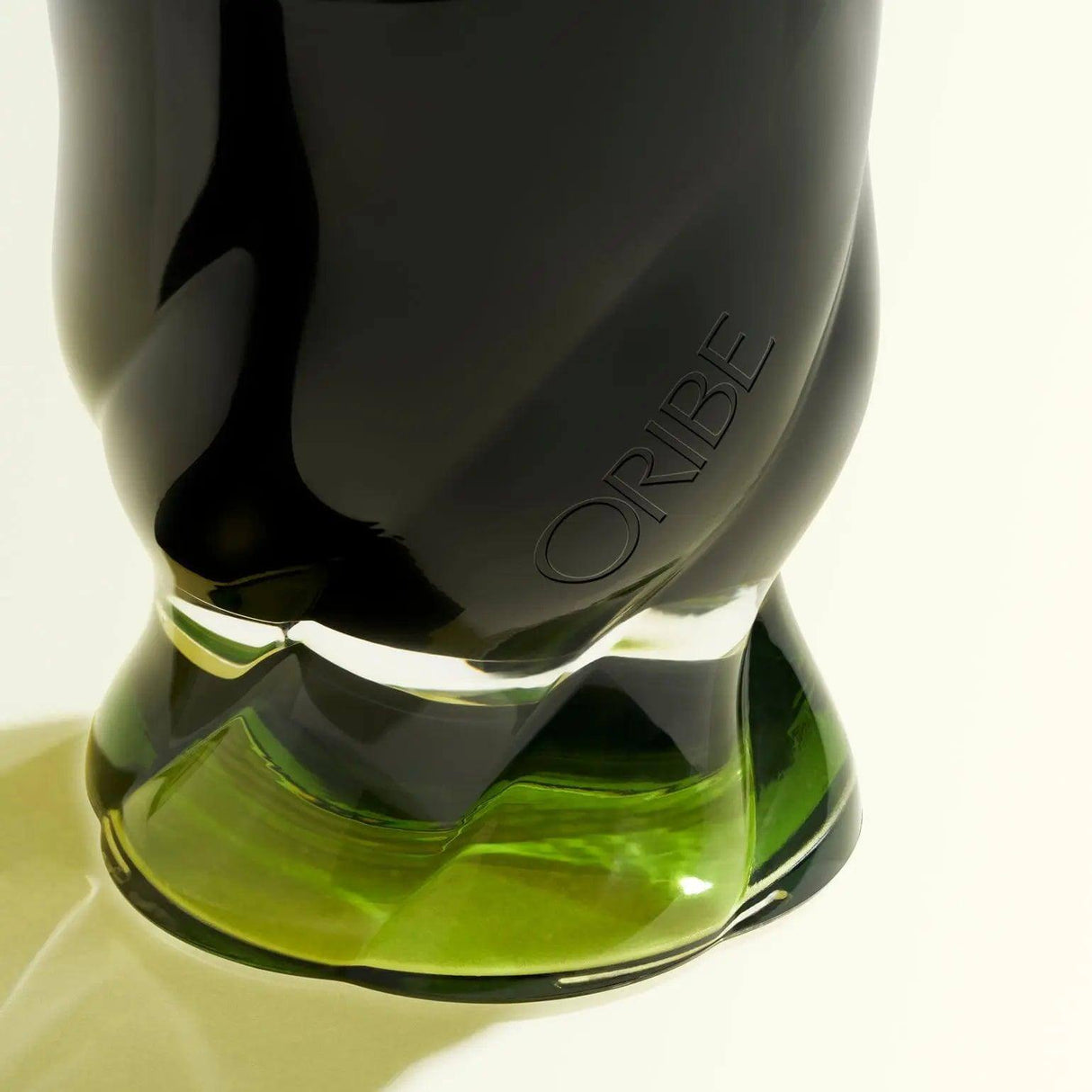 Close-up of Oribe Desertland candle in sculpted green glass holder, reflecting elegance and luxury in home decor.