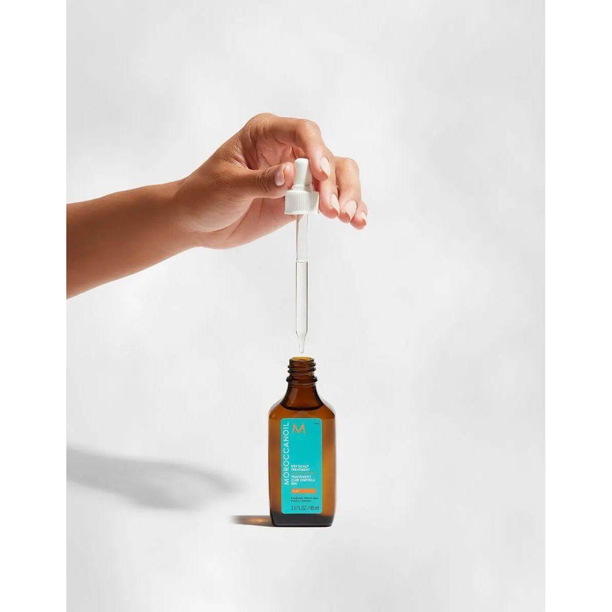 Hand holding dropper above Moroccanoil Dry-No-More Professional Scalp Treatment for dry scalp care.