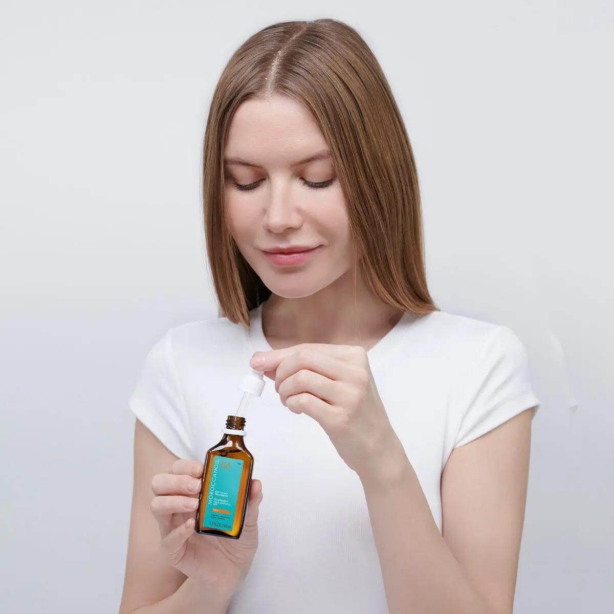Woman using Moroccanoil Dry-No-More Professional Scalp Treatment for dry scalp hydration and rejuvenation.