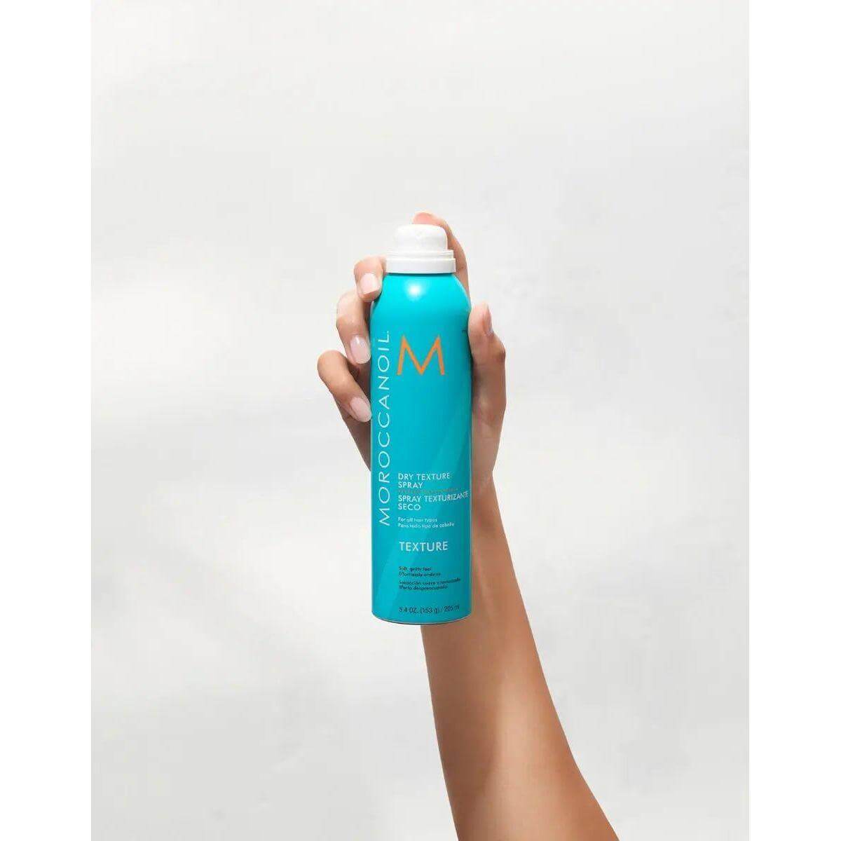 Hand holding Moroccanoil Dry Texture Spray for volume and hold, infused with argan oil.