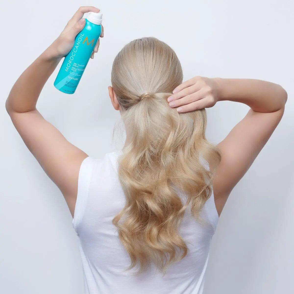 Woman using Moroccanoil Dry Texture Spray for textured waves and volume, creating an effortless hairstyle with argan oil infusion.