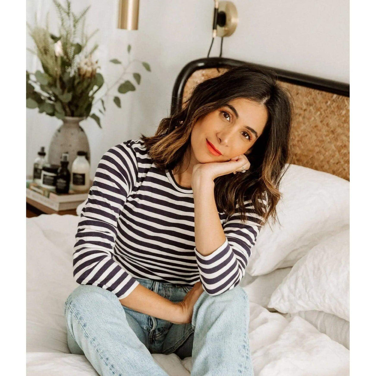 Woman with effortless messy waves hairstyle sitting on a bed in a striped shirt.