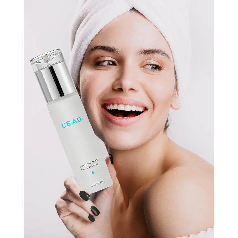 Woman holding Essential Toner by L'EAU, promotes firmer skin, reduces pores and blemishes, infused with Snow Algae and Allantoin.