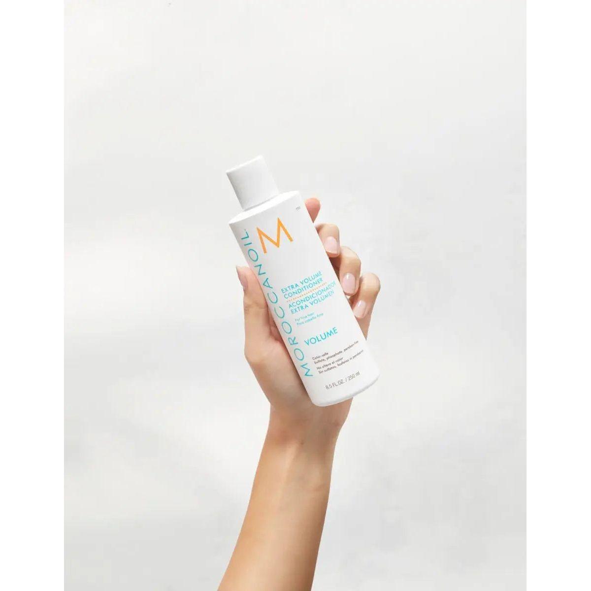 Hand holding Moroccanoil Extra Volume Conditioner bottle against light background
