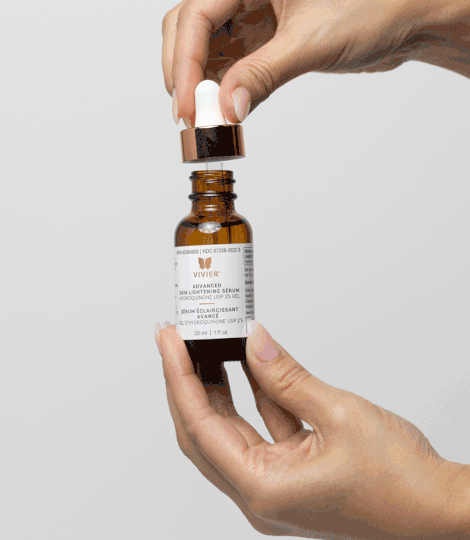 Hands holding Vivier Advanced Skin Lightening Serum bottle with dropper. Potent serum for reducing dark spots and signs of aging.