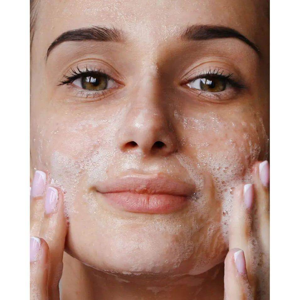 Woman applying exfoliating face cleansing foam with natural ingredients, ensuring deep skin cleanse and refreshed complexion.