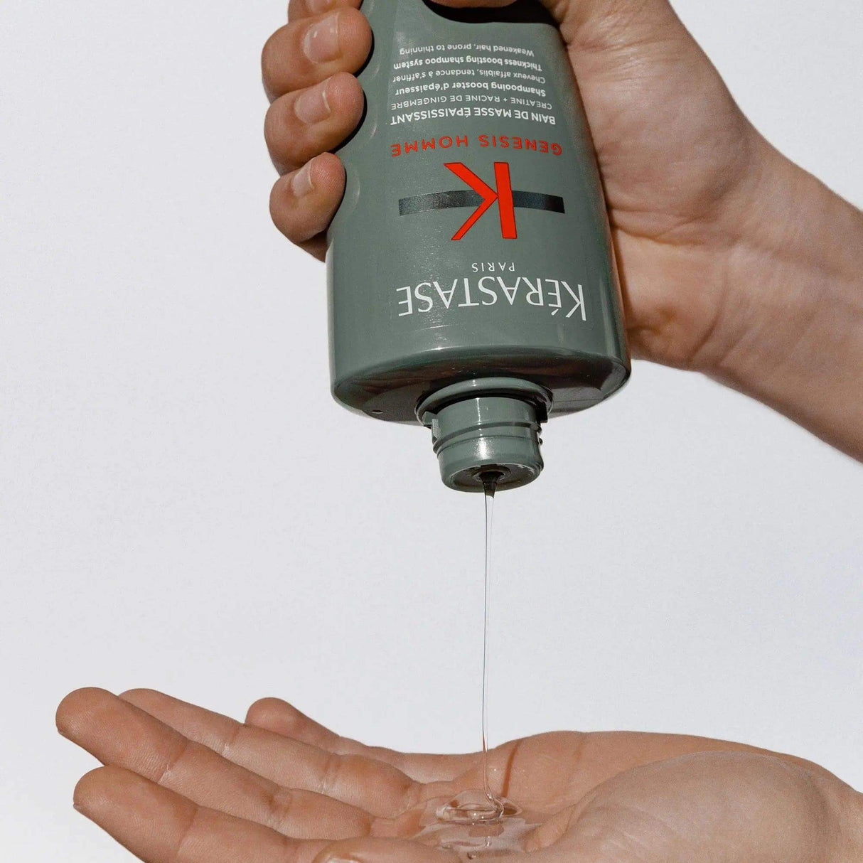 Pouring Kérastase Genesis Homme Bain De Masse Épaississant Shampoo into hand for hair thickening and cleansing.