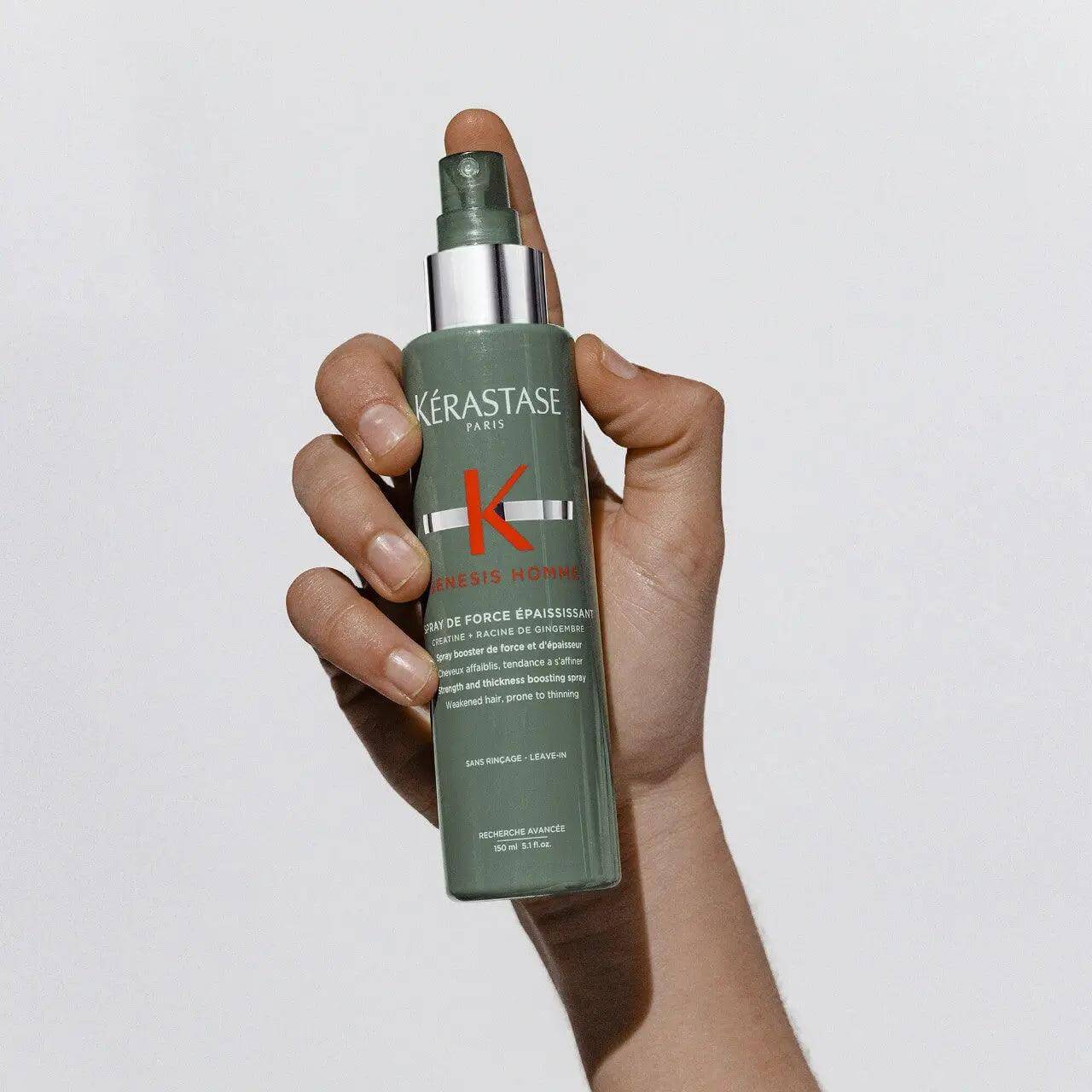 Hand holding Kérastase Genesis Homme Spray de Force Épaississant for men's thinning hair, offers lightweight hold and thickening effect.
