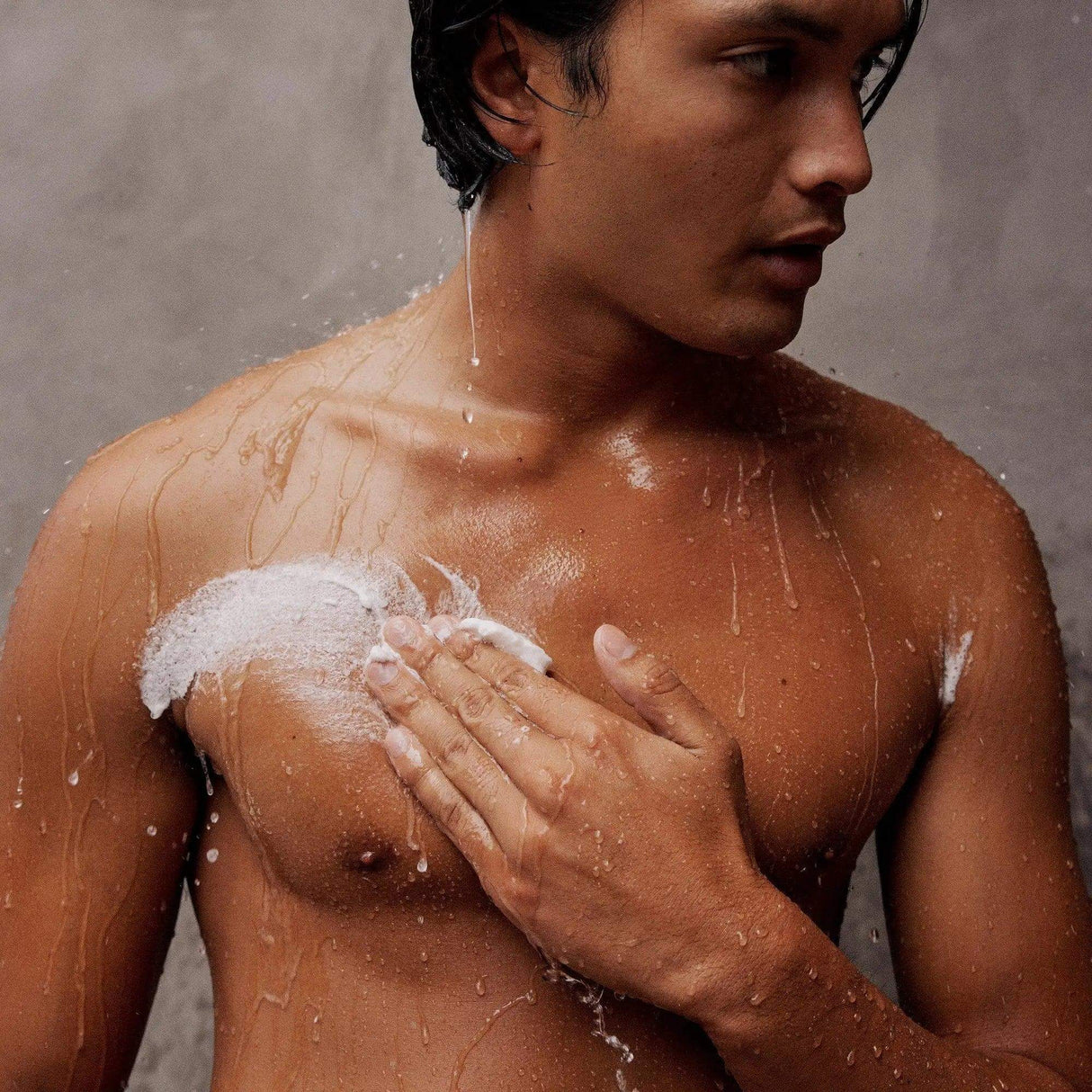 Person using Gilded Woods Body Scrub in shower, applying product to exfoliate and hydrate skin for smoothness and protection.