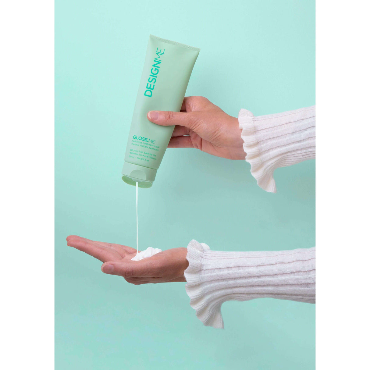Gloss.Me Hydrating Treatment Mask being dispensed onto hand, showcasing its creamy texture and sleek packaging against a mint green background.