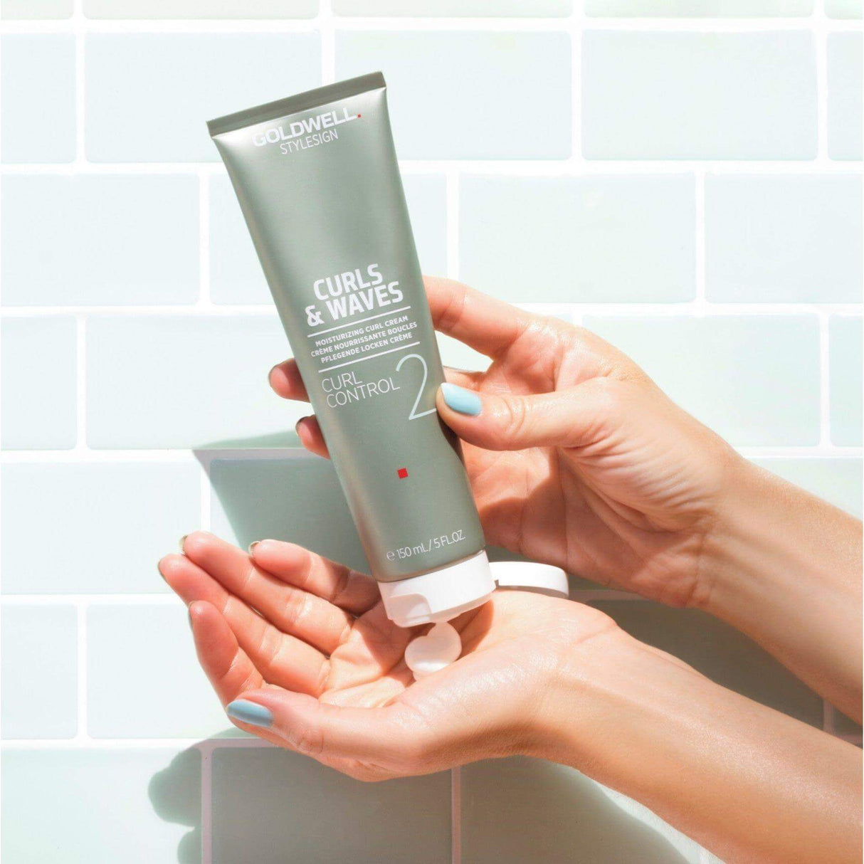 Hands applying Goldwell Curls & Waves Curl Control Moisturizing Curl Cream, ideal for nourishing and defining shiny, bouncy curls.