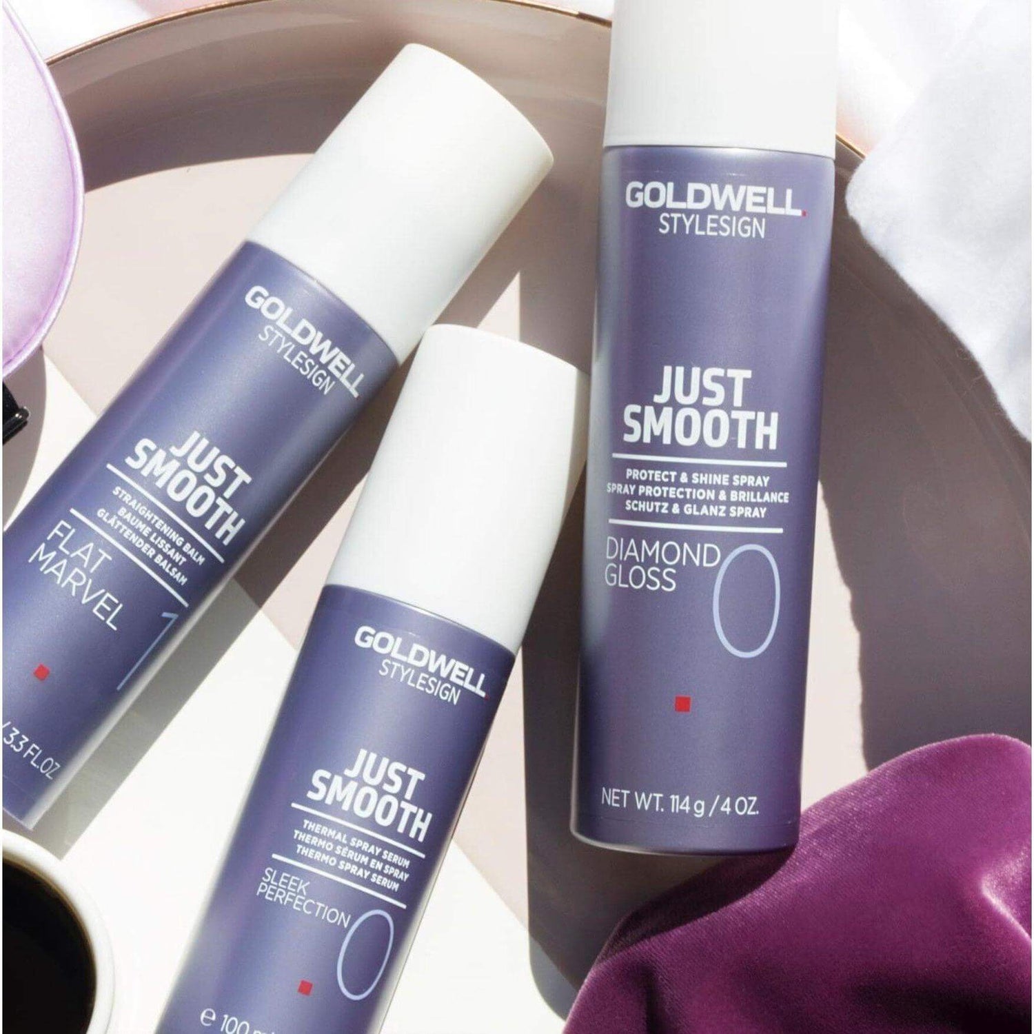 Goldwell Just Smooth Sleek Perfection Thermal Spray Serum and other products on a reflective surface.