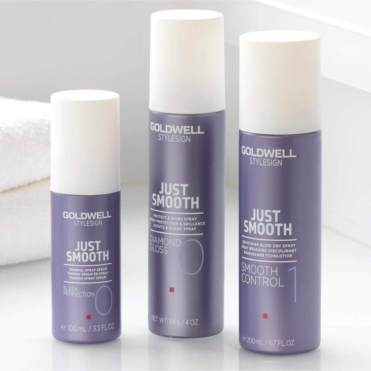 Goldwell Just Smooth product lineup including Sleek Perfection Thermal Spray, Diamond Gloss Spray, and Smooth Control Spray on bathroom counter.