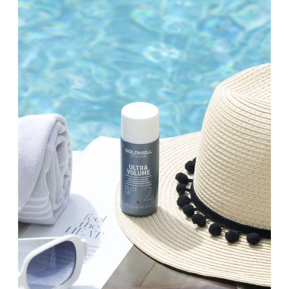 Goldwell StyleSign Ultra Volume Dust Up Volumizing Powder beside a pool with hat and sunglasses, enhancing hair volume.
