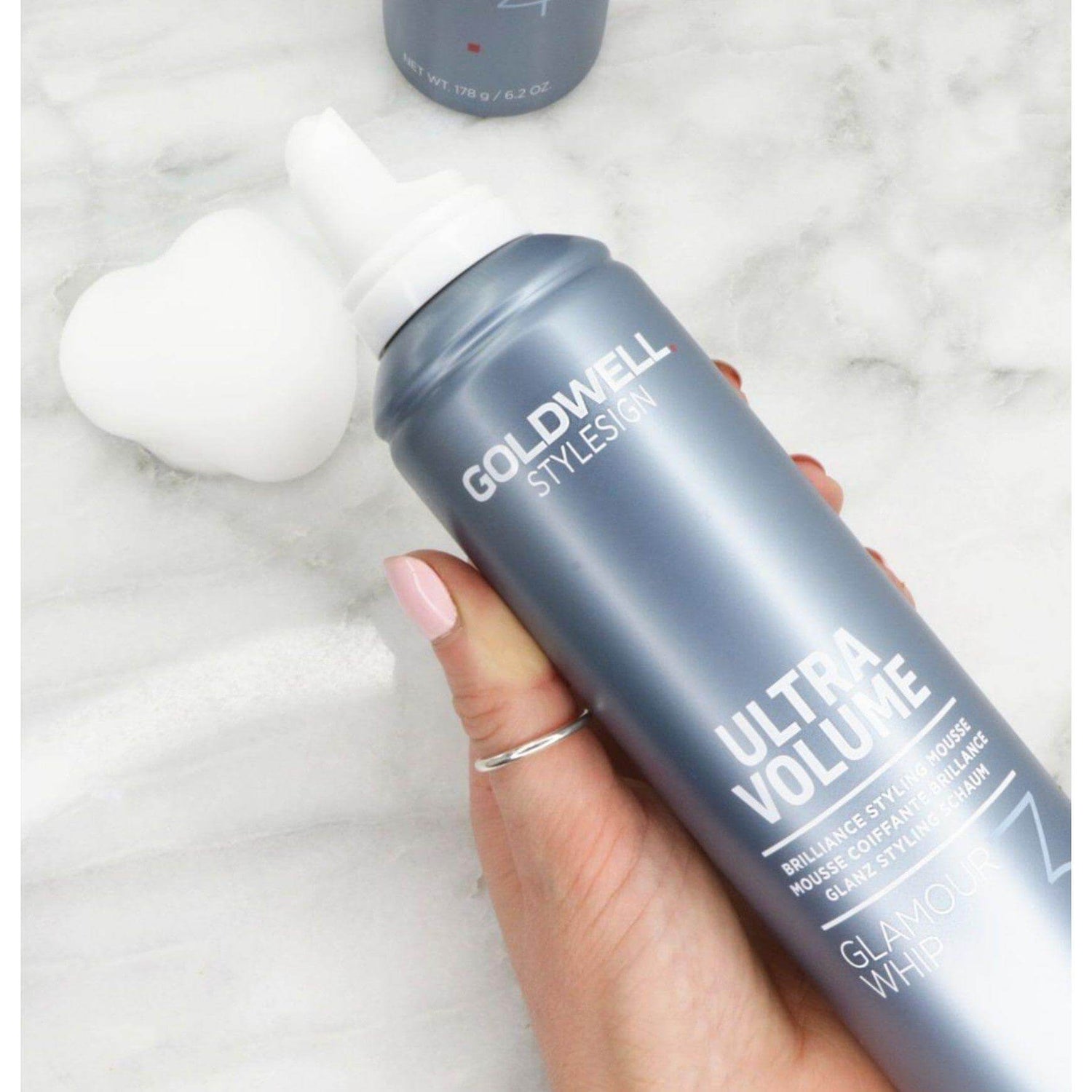 Goldwell Stylesign Ultra Volume Glamour Whip mousse can held by hand on marble surface.
