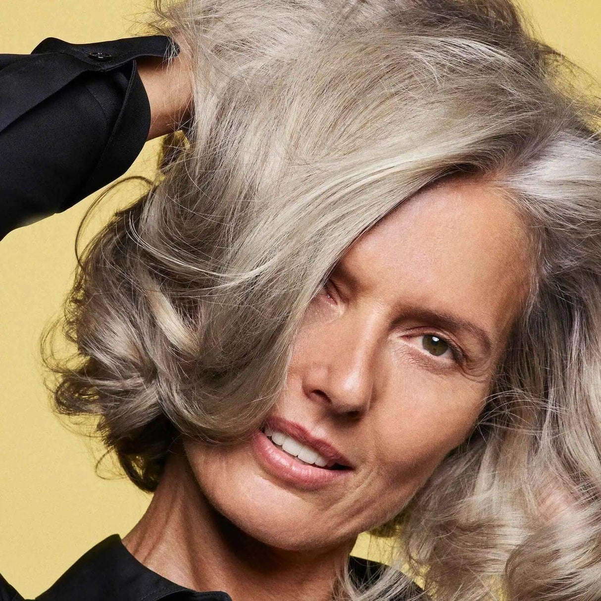 Woman with healthy, voluminous hair styled in loose waves, promoting Hair Alchemy Fortifying Treatment Serum benefits.