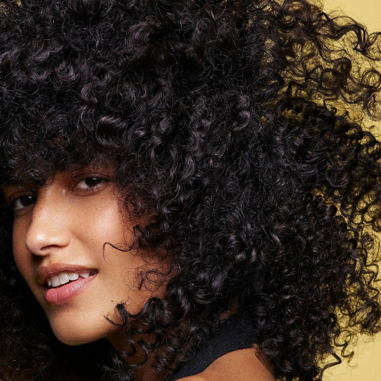 Woman with lush curly hair demonstrating healthy hair appearance after using Hair Alchemy Strengthening Masque.