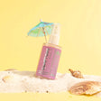 Hamptons Dry Shimmering Oil bottle in sand with mini umbrella, pink color, 2 oz, organic coconut oil, watermelon lemonade scent.