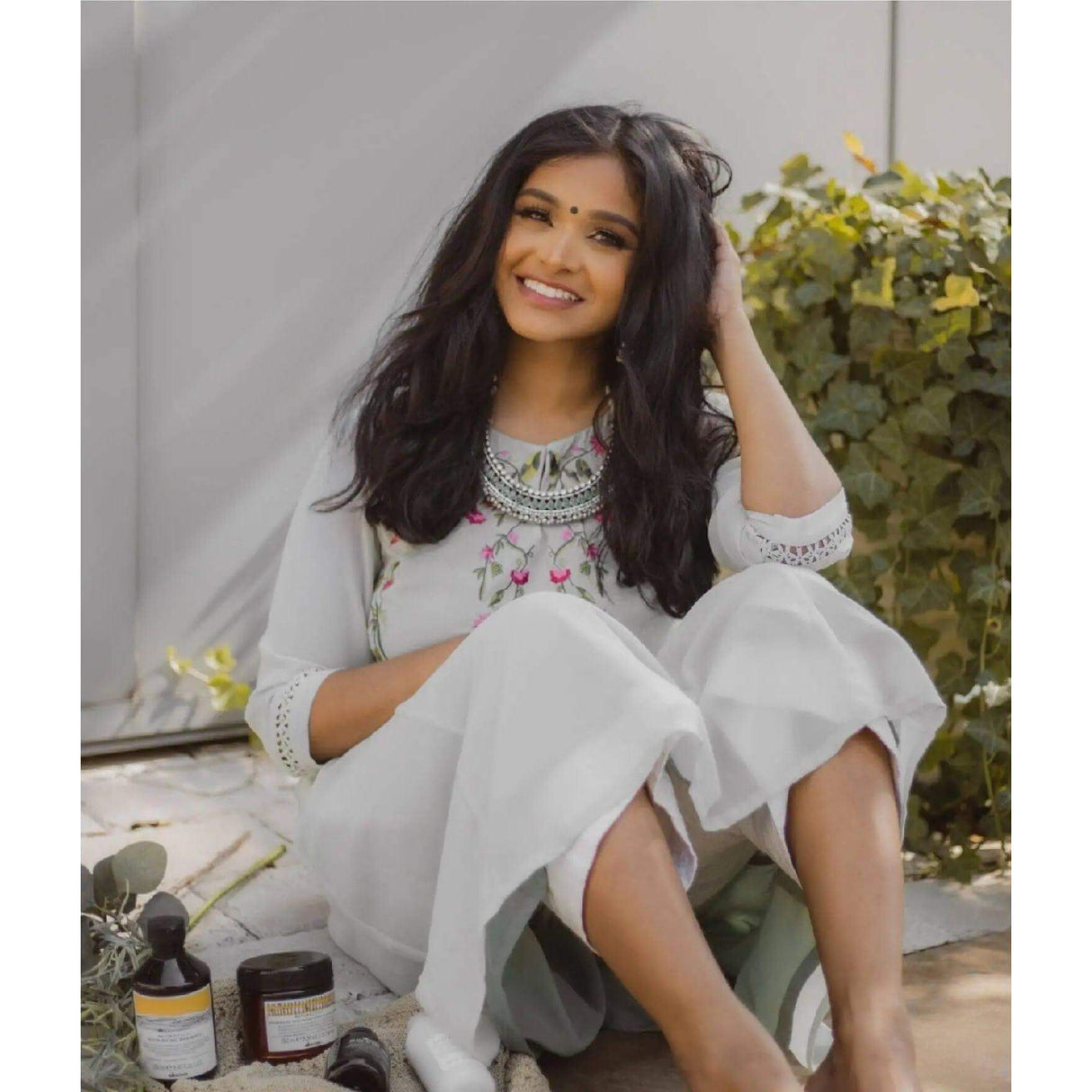 Woman with natural waves sitting outdoors with Davines Heatless Natural Waves Set on the ground, showcasing hair care products.