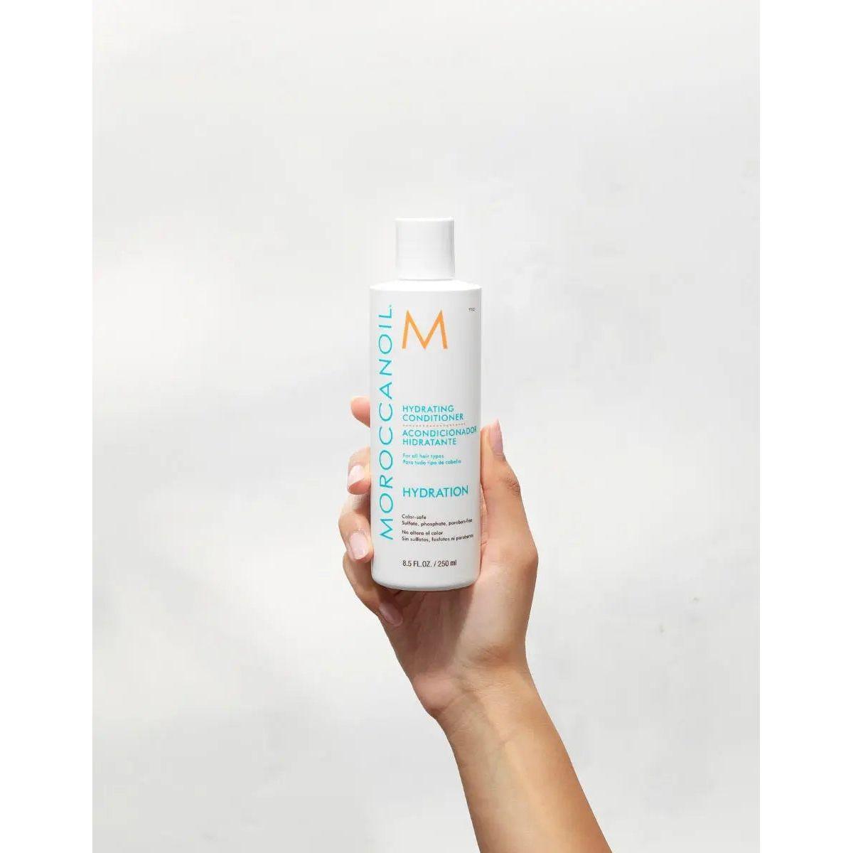 Hand holding Moroccanoil Hydrating Conditioner with argan oil, vitamins A, E, and red algae for moisture and detangling, 250ml bottle.