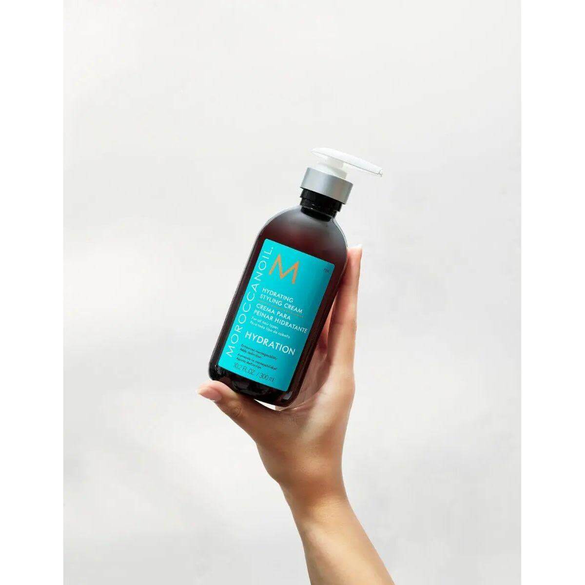 Hand holding Moroccanoil Hydrating Styling Cream bottle for moisturizing and frizz control.