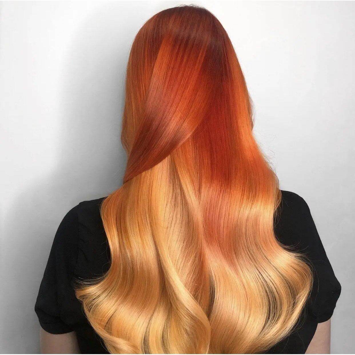 Long, wavy hair with vibrant red and orange ombre color, showcasing a smooth and glossy finish from using a styling and protection duo.