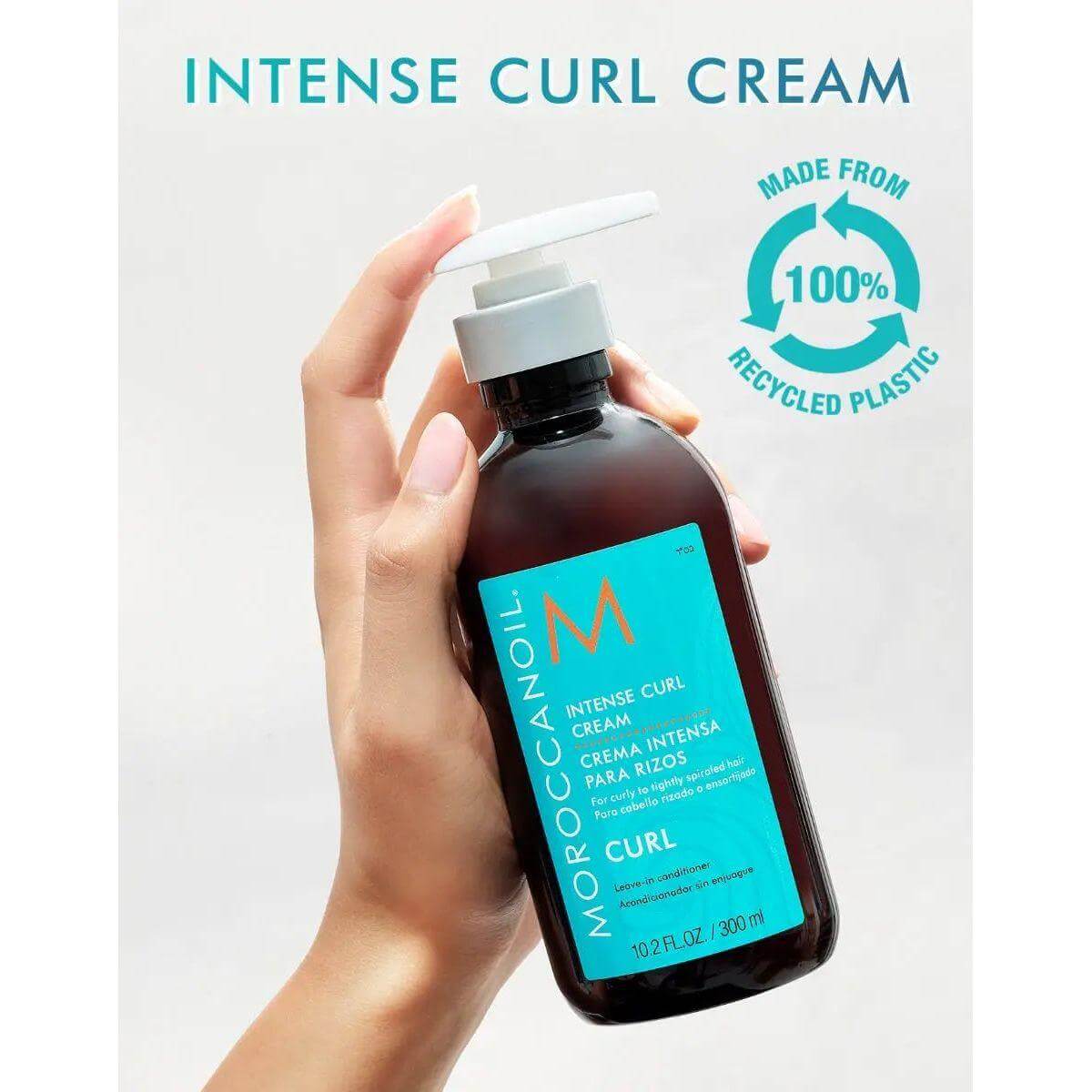 Hand holding Moroccanoil Intense Curl Cream bottle, made from 100% recycled plastic, for hydrated and frizz-free curls.