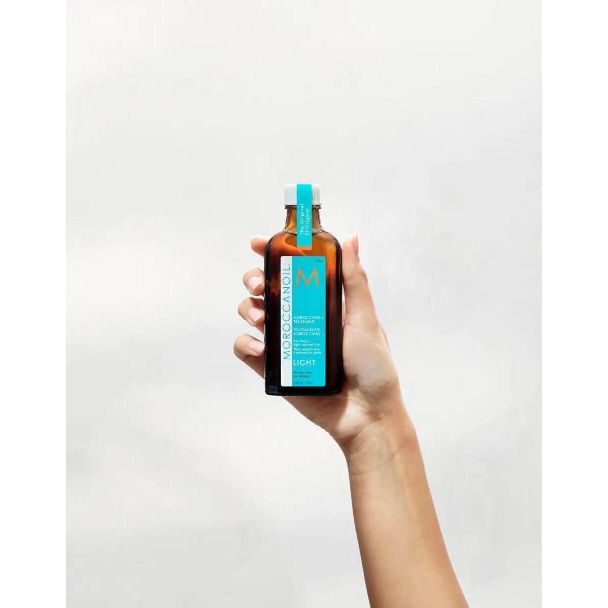 Hand holding Moroccanoil Light Treatment bottle for fine hair, infused with argan oil, designed to control frizz and enhance shine.