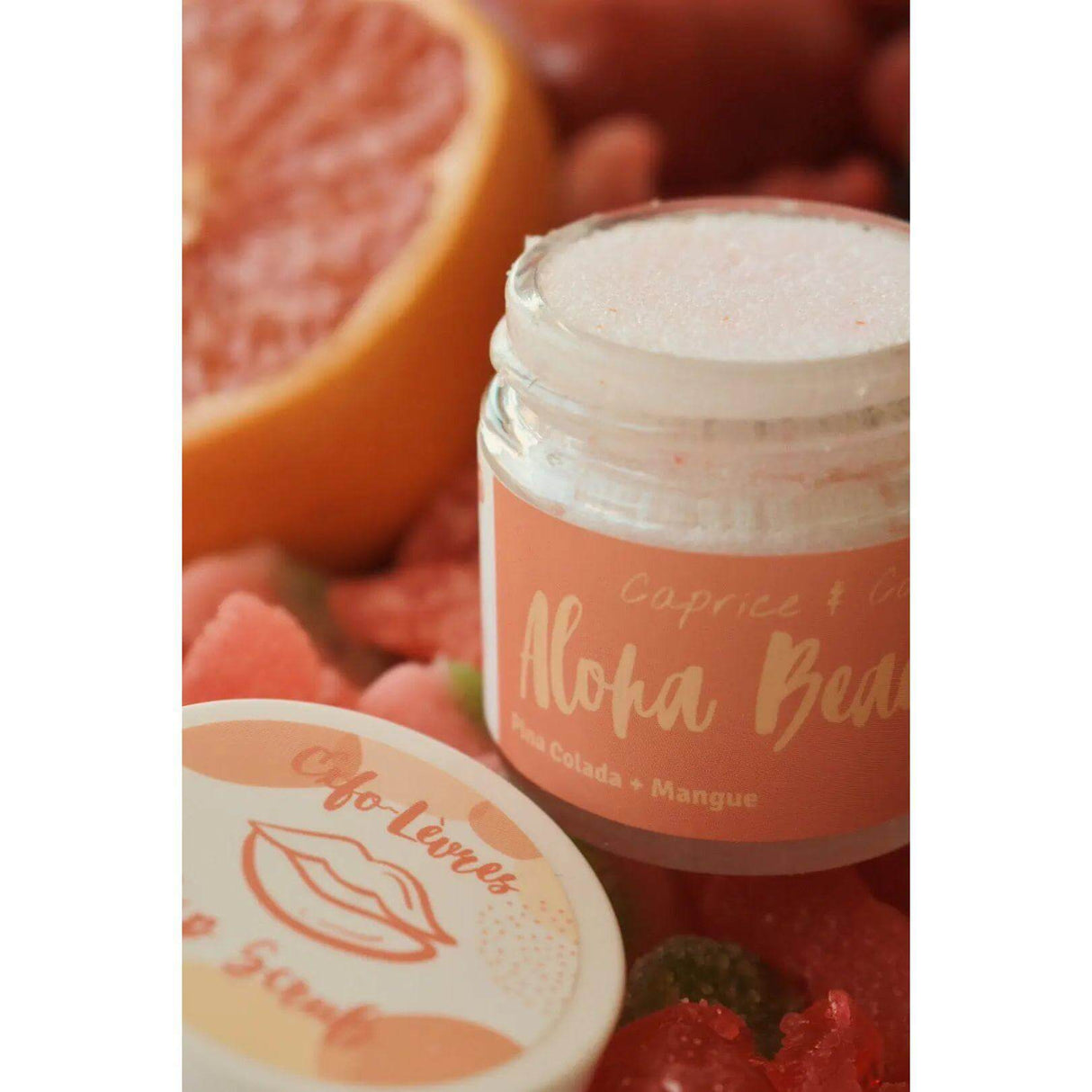 Aloha Beaches Lip Scrub jar with lid, featuring Pina Colada and Mango flavor, surrounded by fruit slices, 1 oz size.