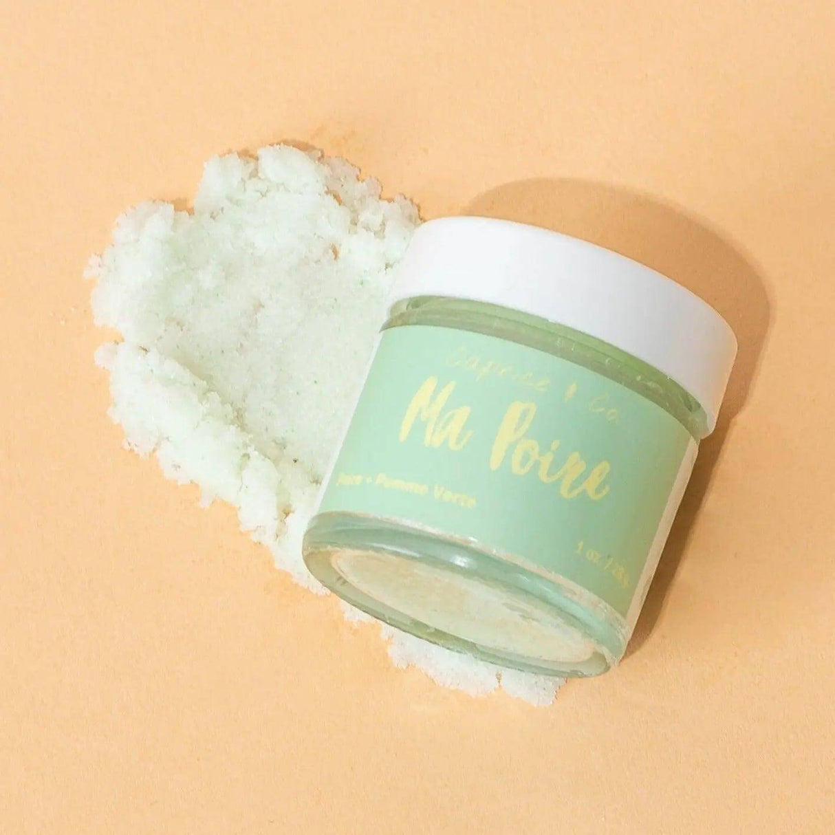 Ma Poire lip scrub jar with sugar exfoliant, featuring pear and green apple flavors, on a peach background.