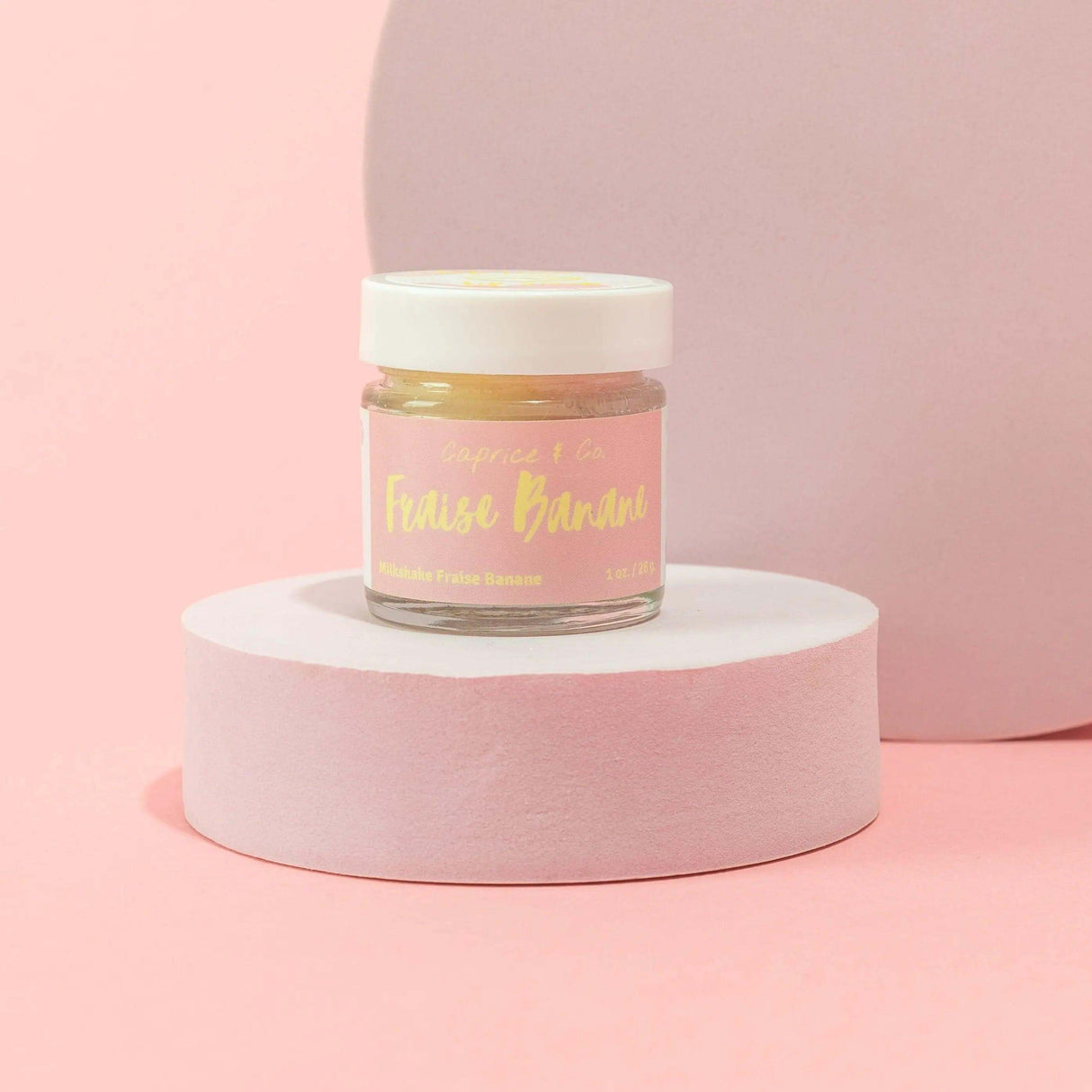 Strawberry Banana Lip Scrub 1 oz jar, gentle exfoliator with sugar, jojoba oil, shea butter on a pastel pink background.