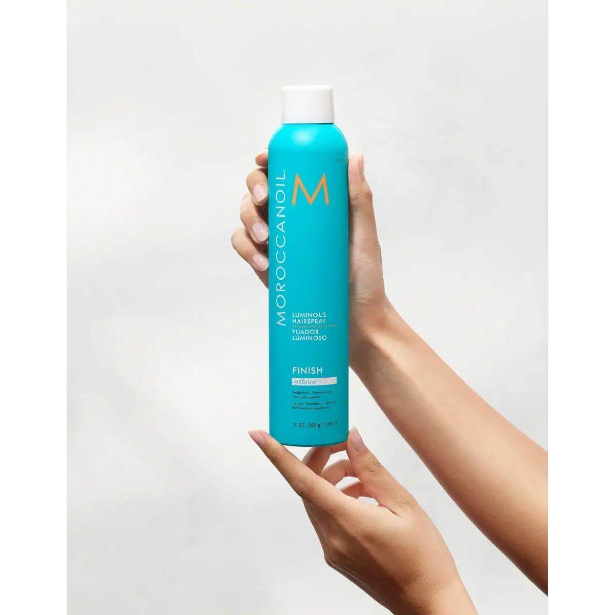 Moroccanoil Luminous Medium Finish Hairspray in a blue bottle being held, offering flexible hold and shine protection.