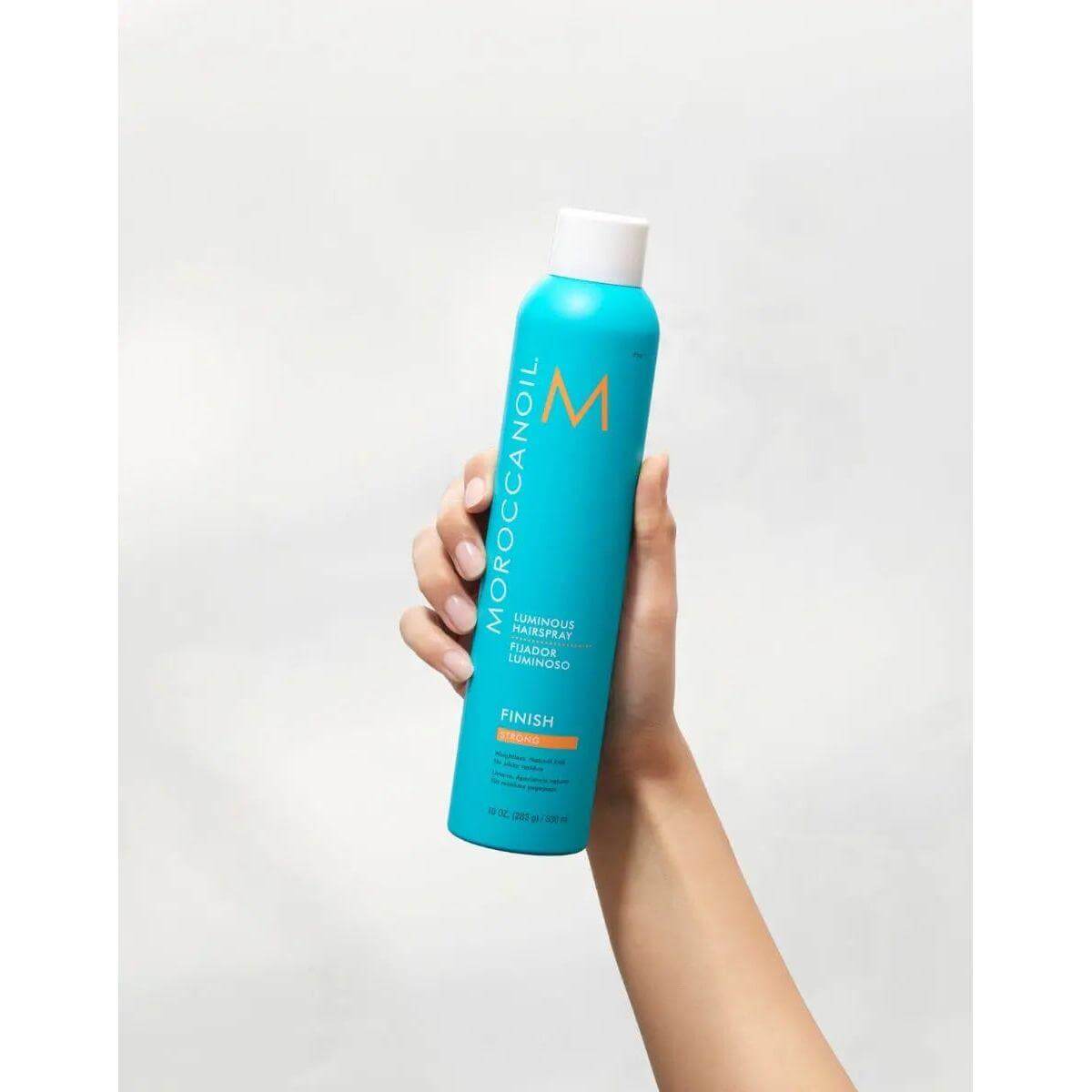 Hand holding Moroccanoil Luminous Strong Finish Hairspray with argan oil for flexible, lasting hold and natural hair styling.