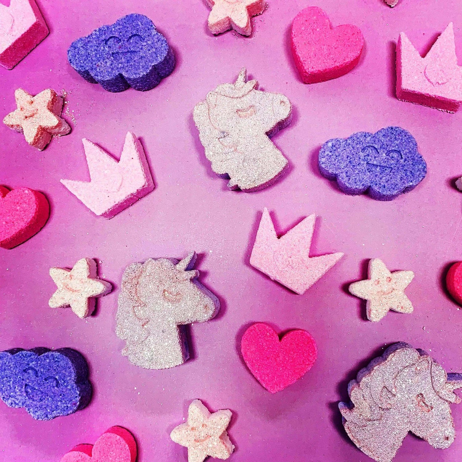 Unicorn, crown, and heart-shaped mini bath bombs on a pink background for Magic Potion collection.