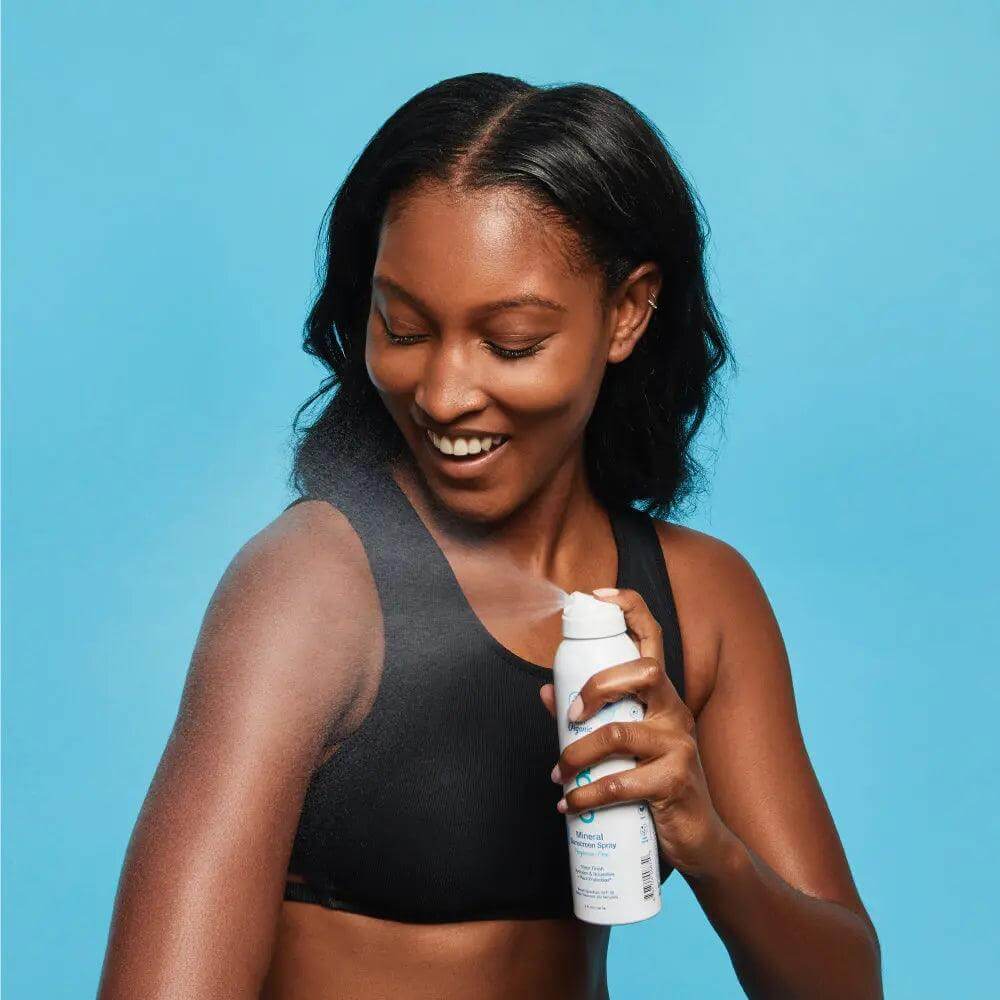 Woman applying organic mineral sunscreen spray SPF 30, fragrance-free, with hydrating, chemical-free protection against free radicals.