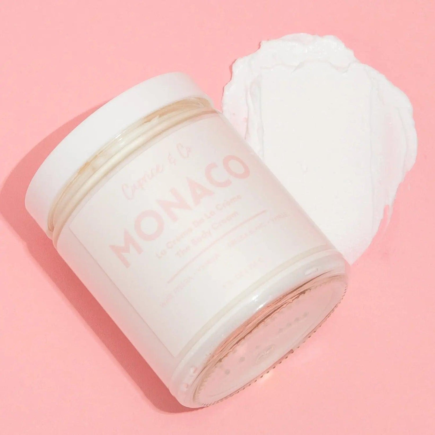 Monaco body cream jar and cream swatch on pink background; scented with white freesia and vanilla, hydrates with coconut and shea butter.