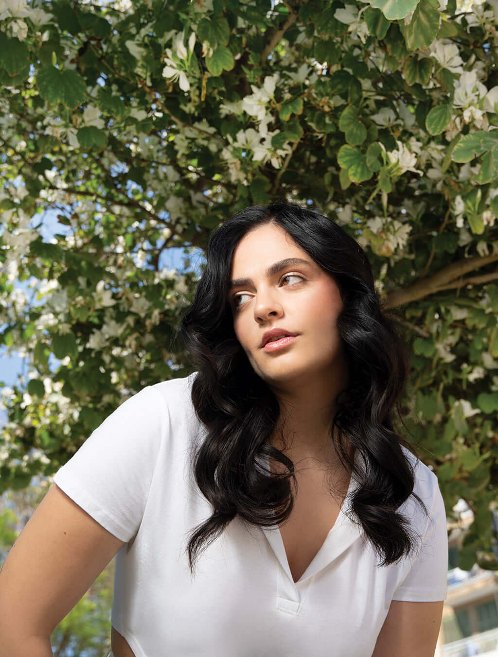 Woman with long, curly hair under a blossoming tree in a white top