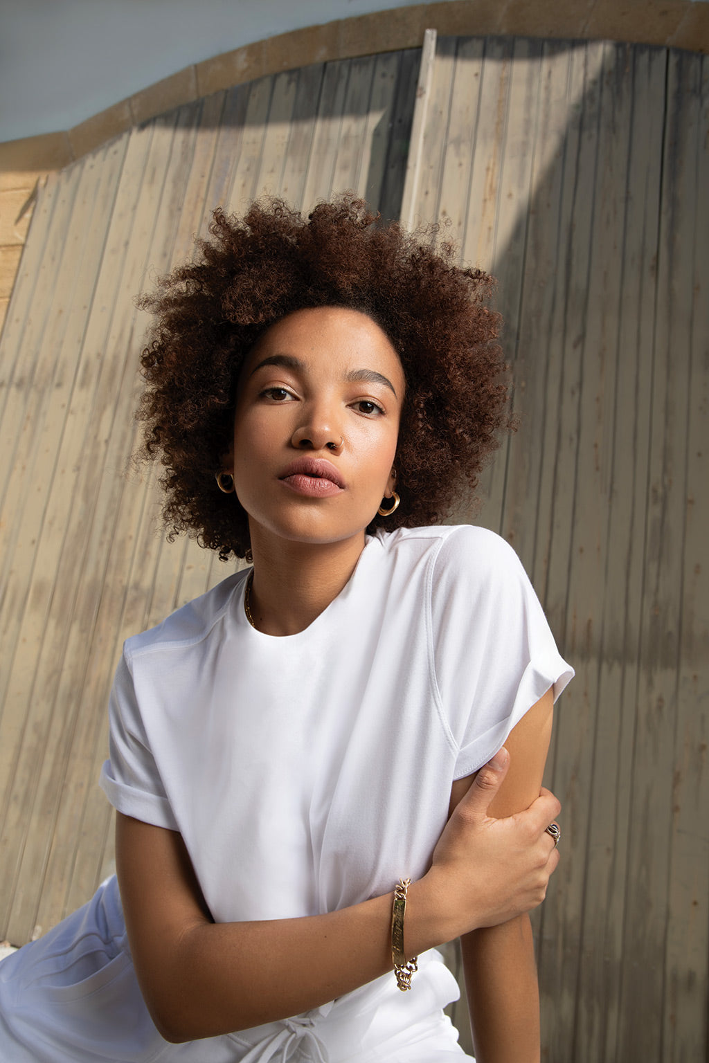 Fashionable woman with natural curls posing outdoors in a white shirt.