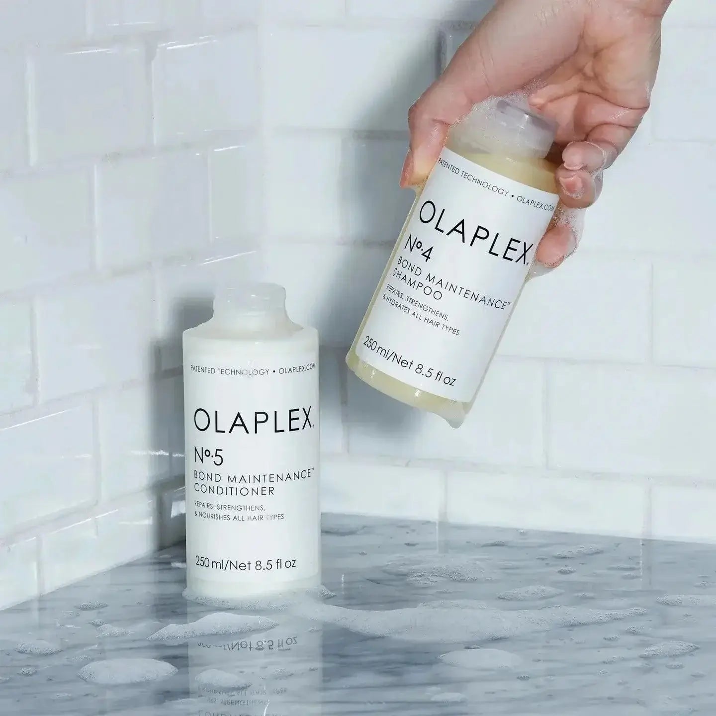 Olaplex Nº.4 Bond Maintenance Shampoo and Nº.5 Conditioner on a marble countertop.