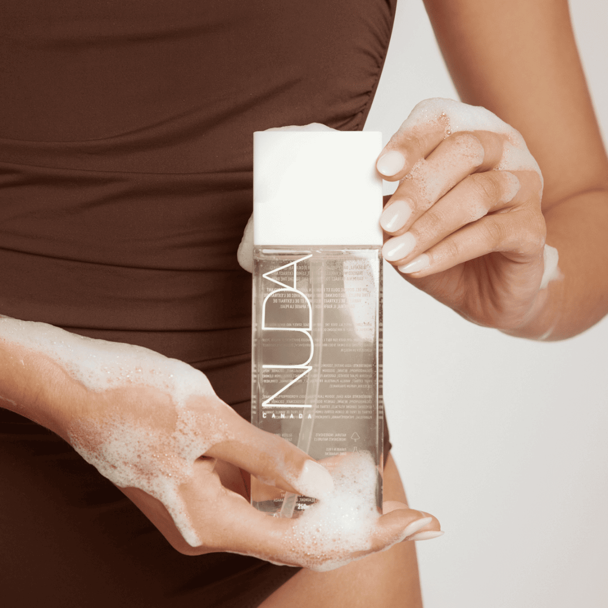 Woman holding a bottle of body wash for sunless tanning with foamy soap bubbles, ideal for maintaining a streak-free tan.