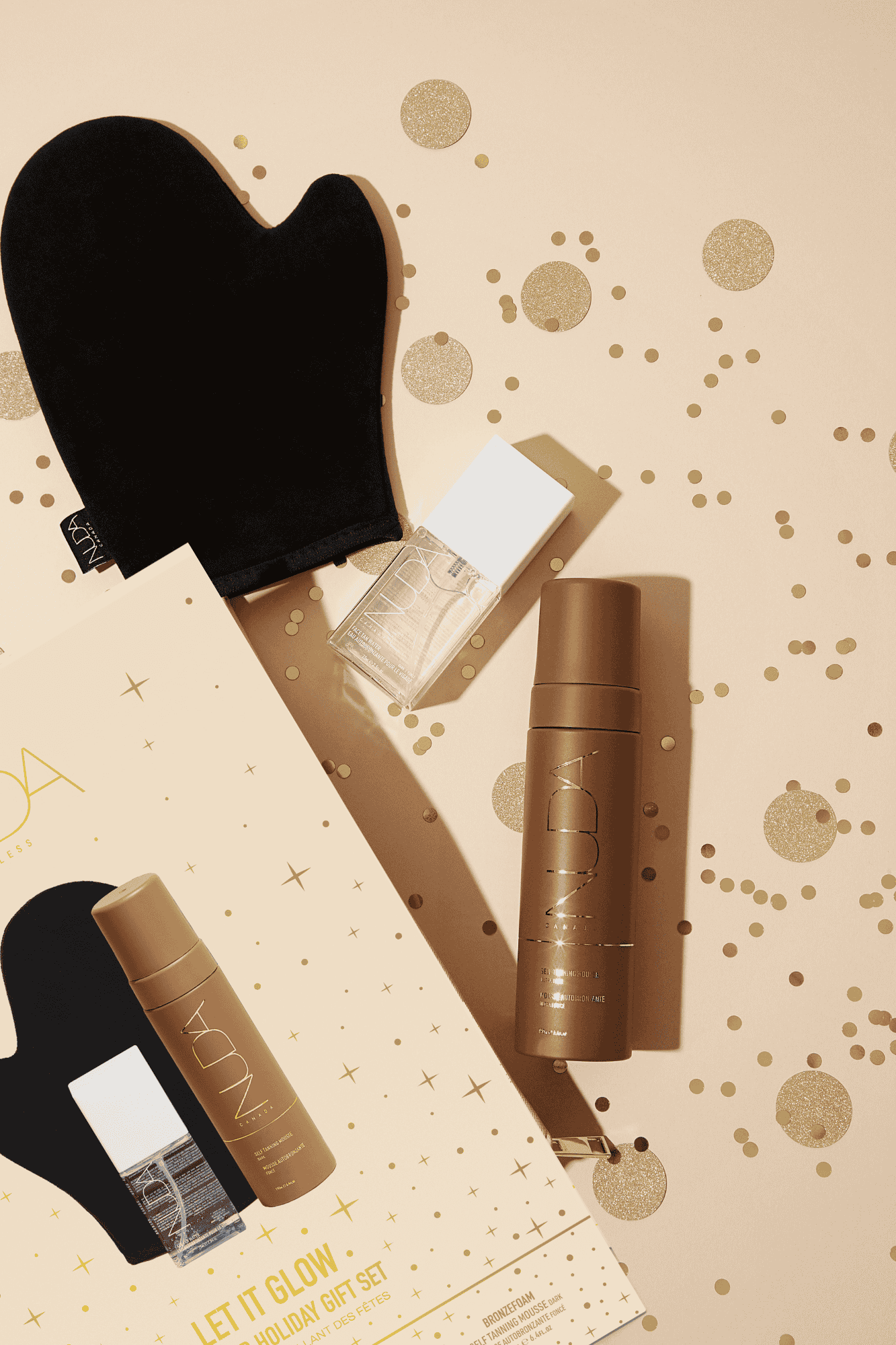 Nuda Bronzed Holiday Gift Set with Dark Tanning Mousse, Mitt, and Face Tan Water on sparkling background.