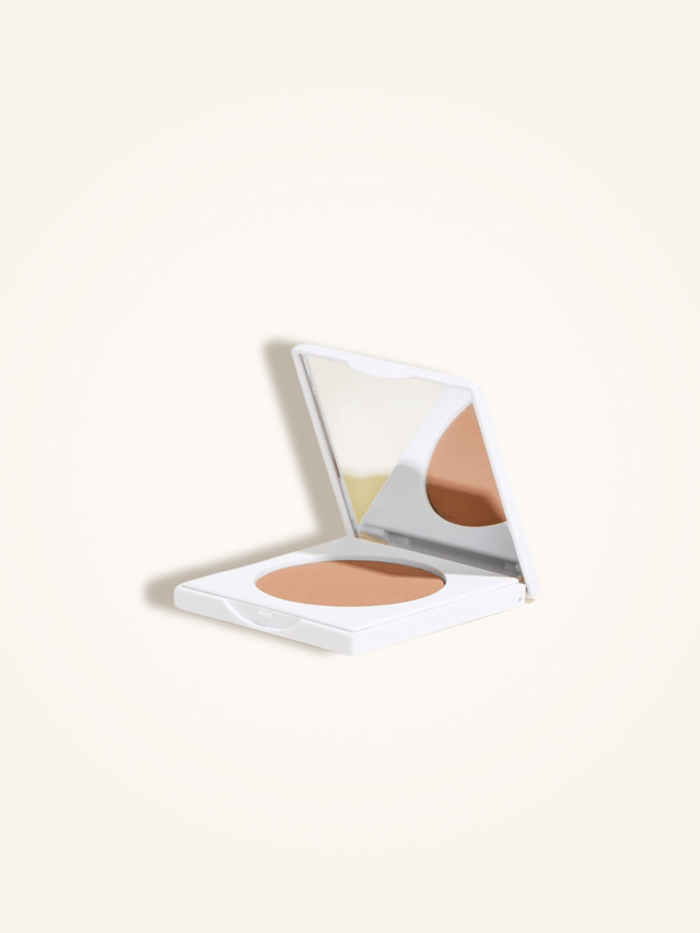 Open compact case of matte bronzing powder with mirror, designed for a natural tan and infused with jojoba, mango, and papaya extracts.