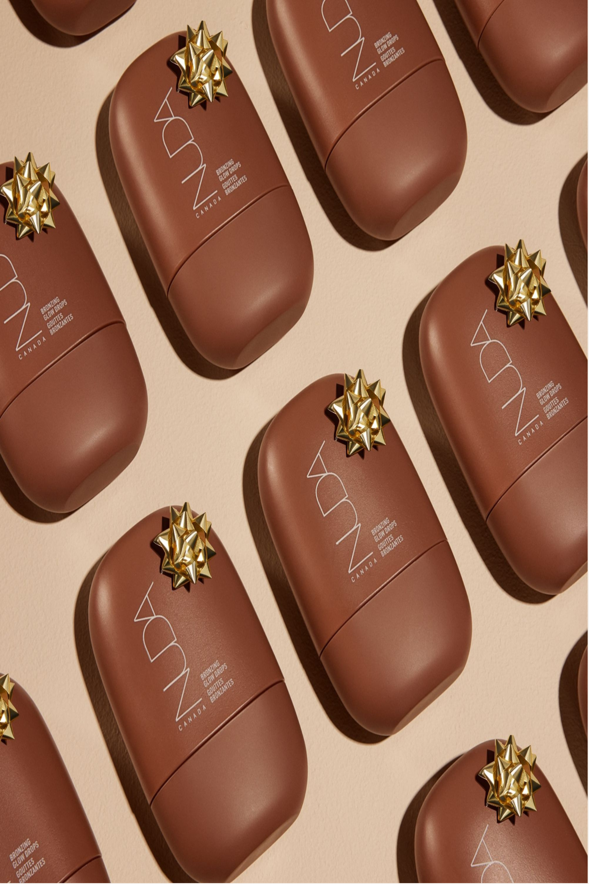 Nuda Bronzing Glow Drops in festive packaging, brown bottles with decorative bows, arranged on a neutral background.