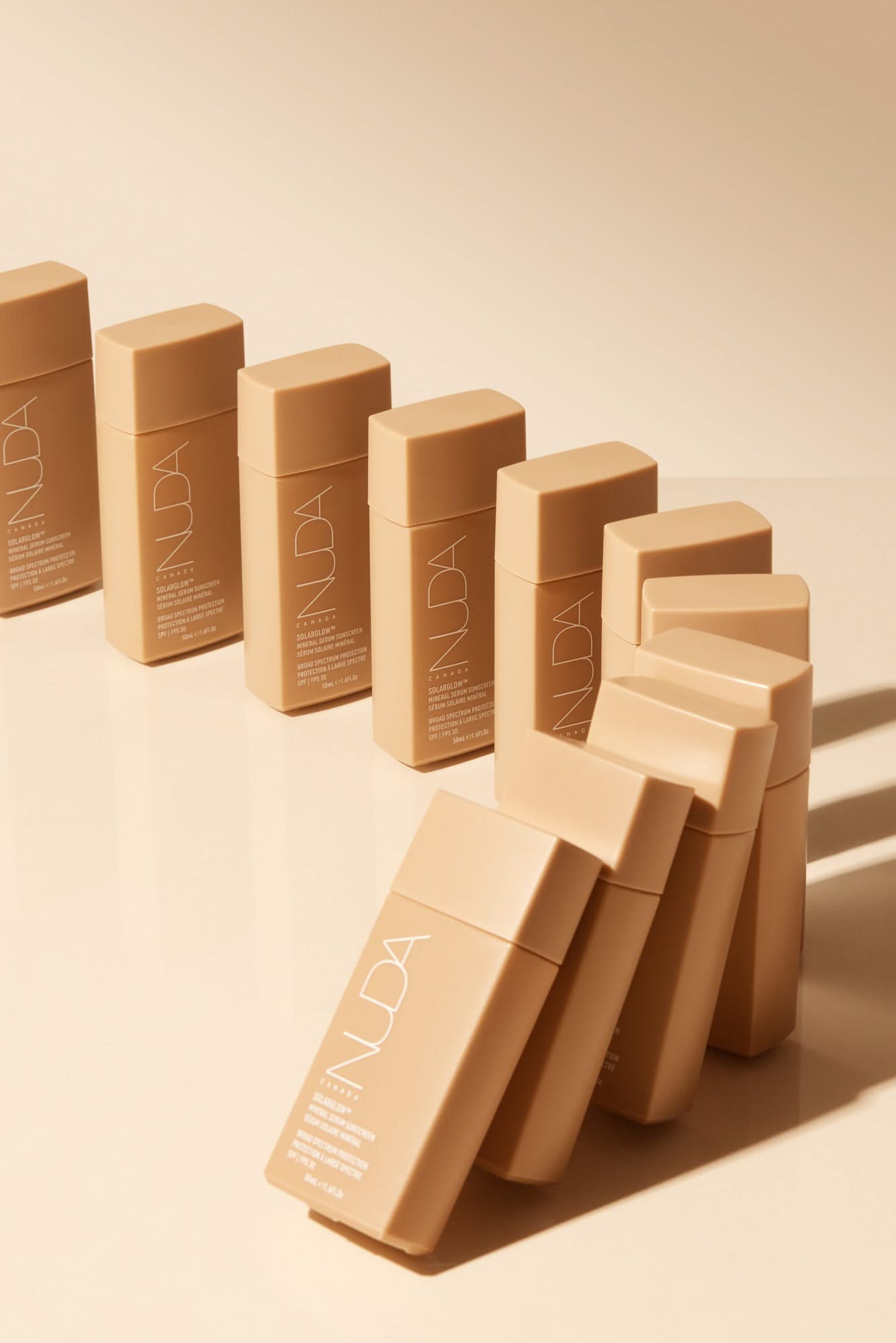 Row of beige rectangular cosmetic bottles with minimalist design on a neutral background